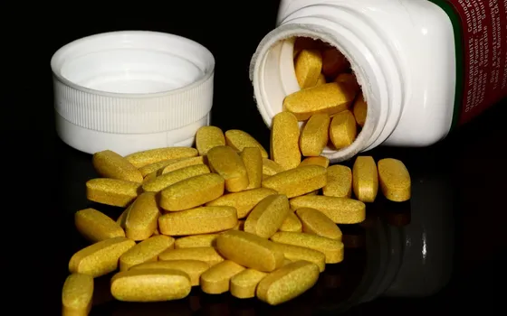 Yellow B vitamin tablets spilling from a white supplement bottle