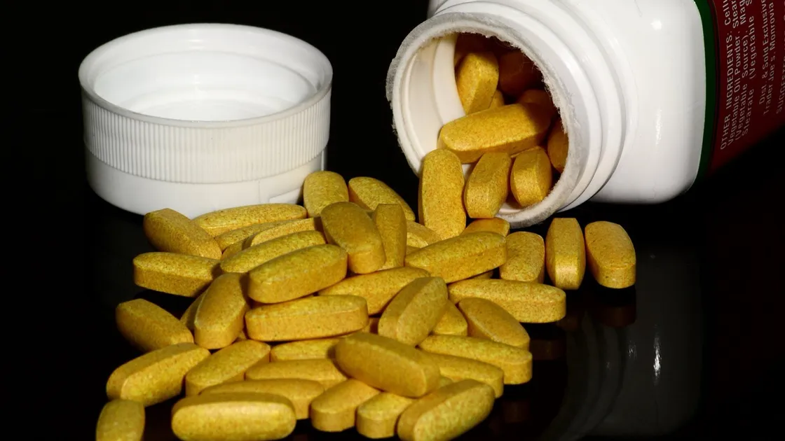 Yellow B vitamin tablets spilling from a white supplement bottle