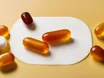Amber CoQ10 softgel capsules beside white prescription-style tablets on a bright surface