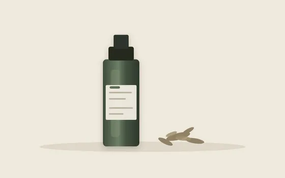 A dark glass dropper bottle beside dried plant material on a plain pale surface