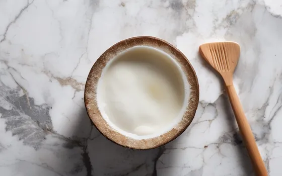 A jar of coconut oil with a wooden spoon, fresh coconut halves and a bamboo toothbrush on a marble surface